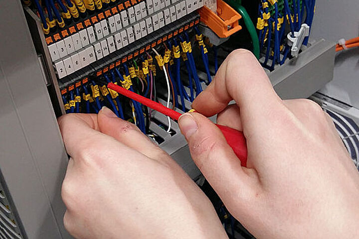 Hand mit Schraubenzieher arbeitet an Elektronik-Bauteil.