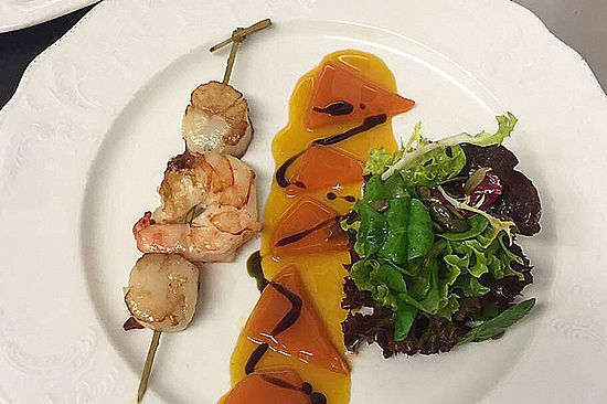 Teller mit Shrimp-/Fisch-Schaschlik-Spieß, geräuchertem Fisch und Salat.