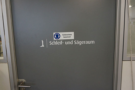 Detailbild: Tür mit Aufschrift „Schleif- und Sägeraum“ sowie mit Warnhinweis „Gehörschutz benutzen“ 