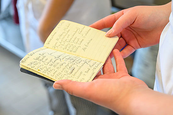 Nahaufnahme: Zwei Hände halten ein kleines Notizbuch mit handschriftlichen Notizen. 