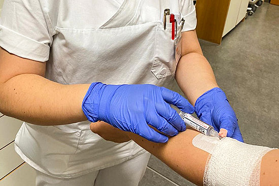 Eine Frau mit Mundschutz und Gummihandschuhen hält eine Kanüle an den Arm einer Patientin. 