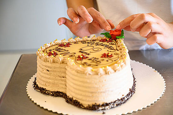 Nahaufnahme: Zwei Hände richten eine dekorierende Zuckerrose auf einer Geburtstagstorte. 