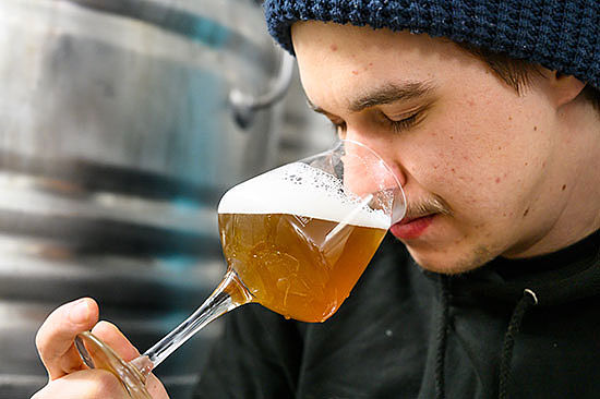 Ein junger Mann hält seine Nase in ein Bierglas, bis kurz vor die Flüssigkeit. Seine Augen sind geschlossen.  